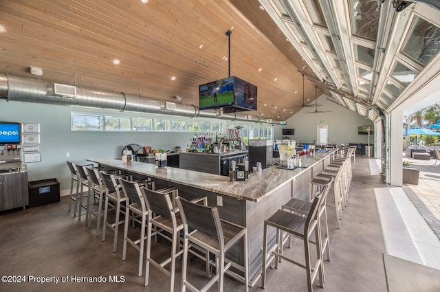 kitchen with ceiling fan, plenty of natural light, light stone counters, and vaulted ceiling