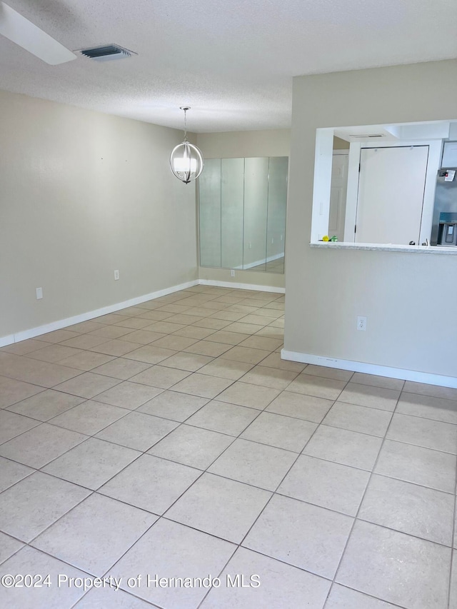 unfurnished room with a notable chandelier, a textured ceiling, and light tile patterned flooring