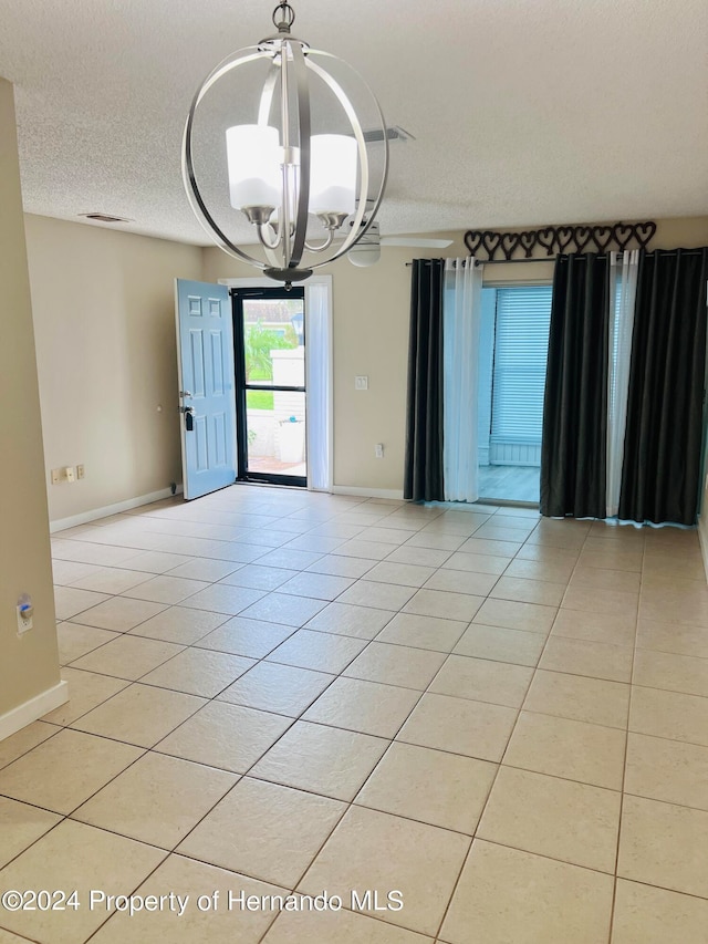 empty room featuring light tile patterned flooring, a textured ceiling, and a notable chandelier