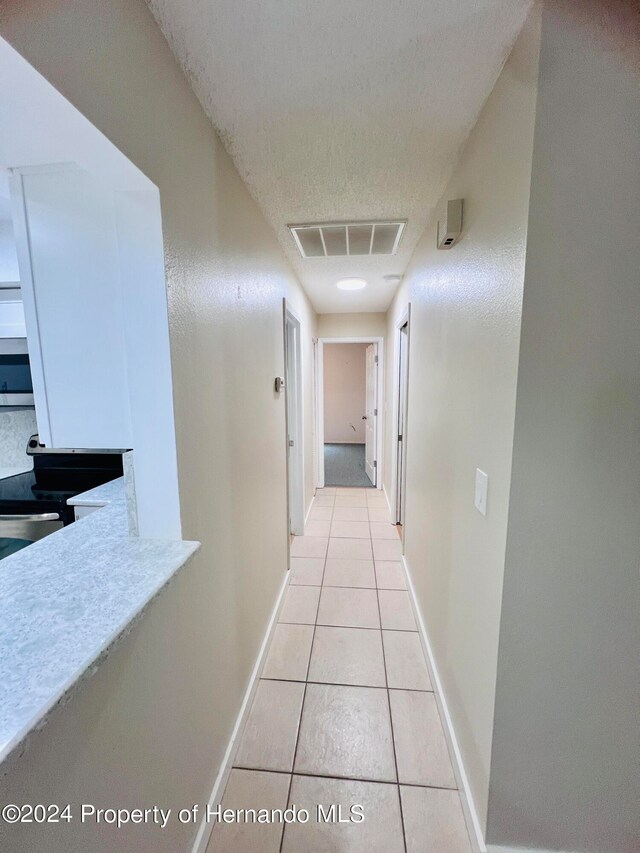 hallway with a textured ceiling and light tile patterned floors