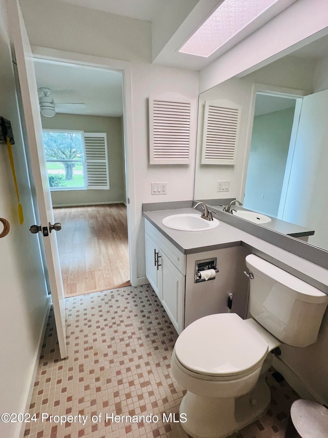 bathroom with vanity, hardwood / wood-style floors, toilet, a skylight, and ceiling fan