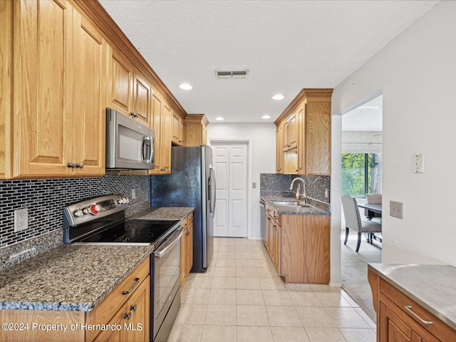 kitchen featuring appliances with stainless steel finishes, a textured ceiling, light tile patterned floors, sink, and dark stone countertops