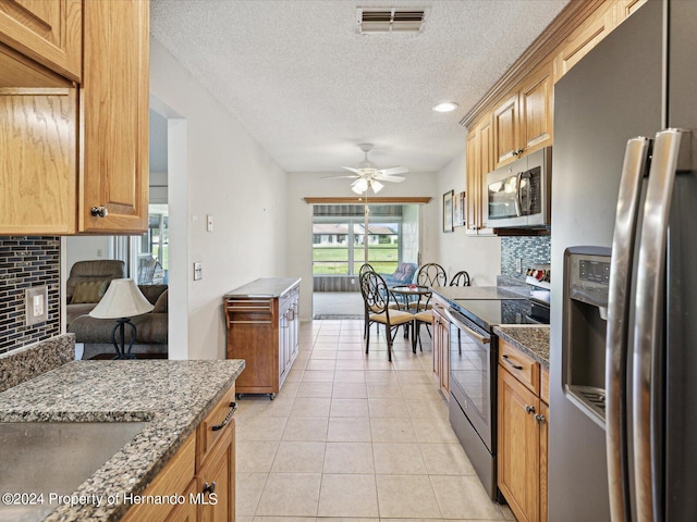 kitchen with stainless steel appliances, dark stone counters, ceiling fan, light tile patterned floors, and decorative backsplash