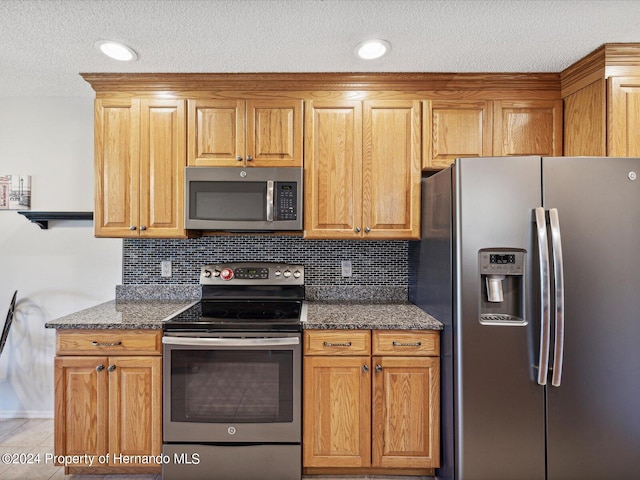 kitchen with stainless steel appliances, dark stone counters, backsplash, and light tile patterned floors