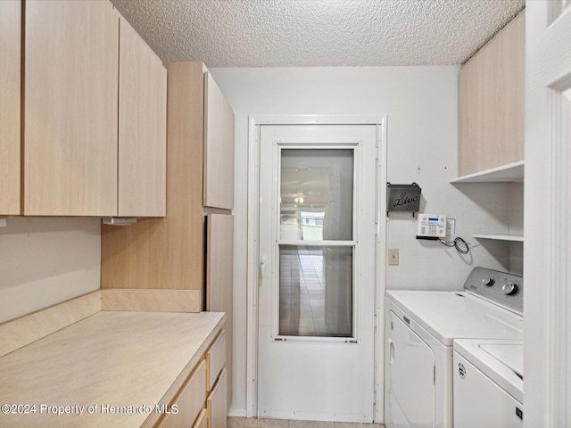 clothes washing area with cabinets, a textured ceiling, and washer and clothes dryer