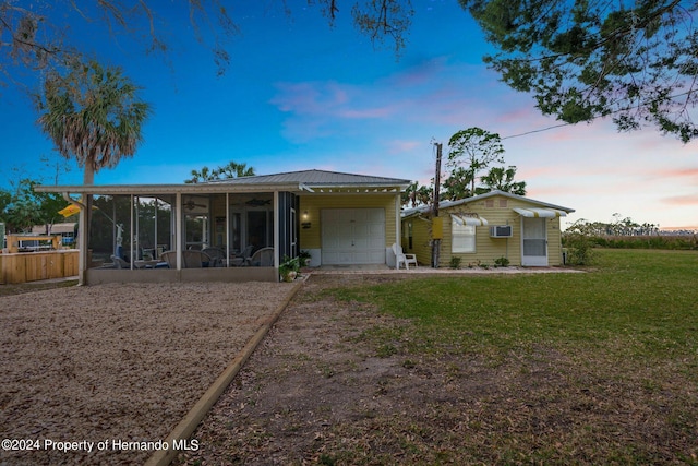 back house at dusk with a garage, a lawn, a sunroom, and a wall mounted air conditioner