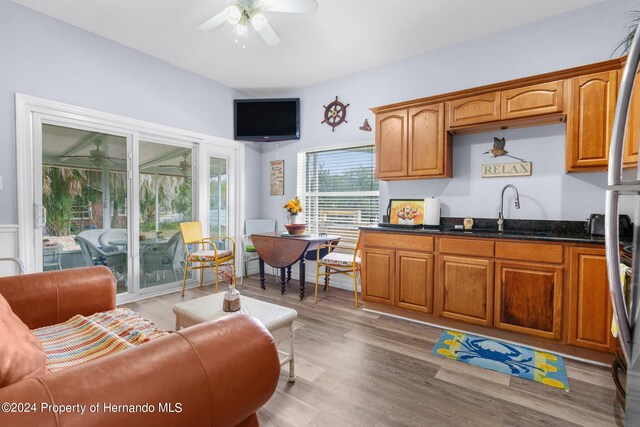 kitchen with dark stone counters, ceiling fan, sink, and light hardwood / wood-style flooring