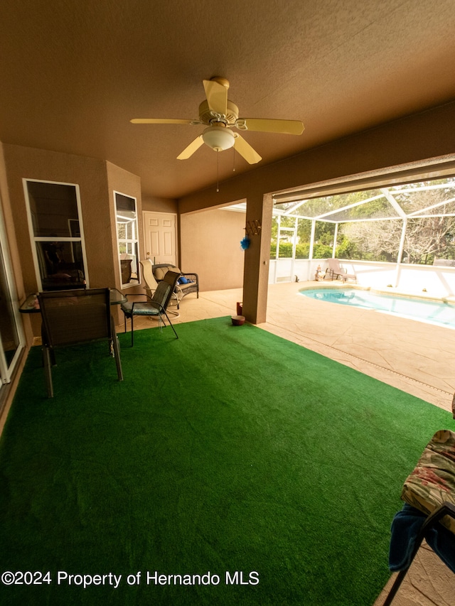 view of yard featuring glass enclosure, ceiling fan, and a patio area