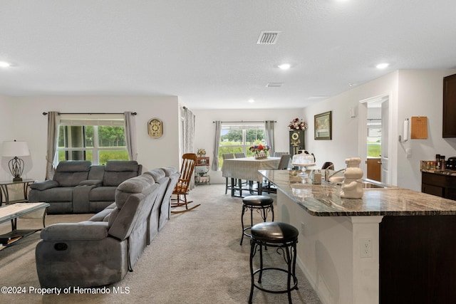 kitchen with a textured ceiling, a center island with sink, light carpet, and a breakfast bar area