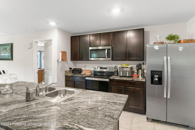 kitchen with stainless steel appliances, stone countertops, dark brown cabinetry, sink, and light tile patterned floors