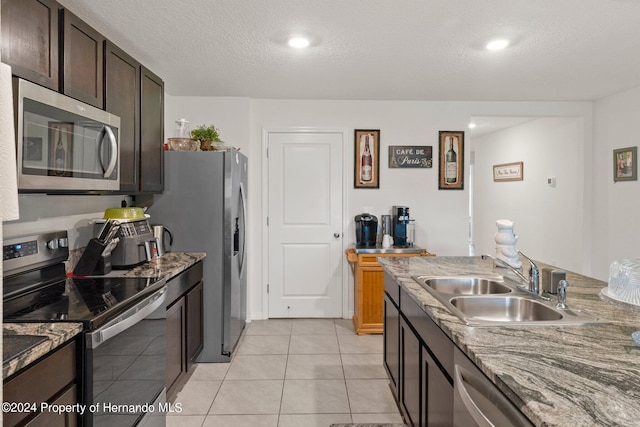 kitchen featuring light tile patterned flooring, stone countertops, sink, appliances with stainless steel finishes, and a textured ceiling