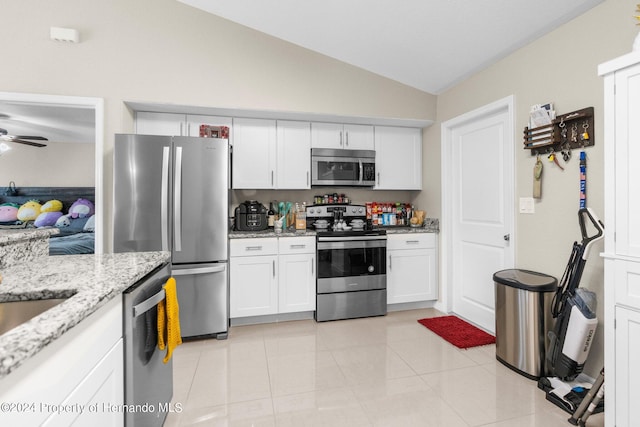 kitchen with lofted ceiling, light tile patterned flooring, light stone countertops, white cabinetry, and appliances with stainless steel finishes