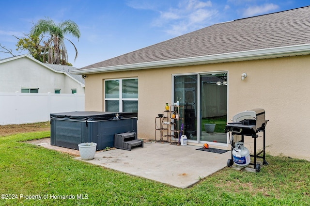 rear view of property with a hot tub, a lawn, and a patio