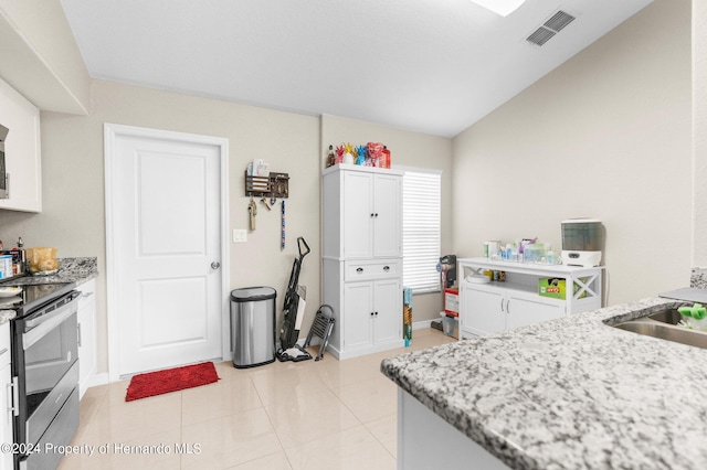 kitchen with vaulted ceiling, white cabinetry, light stone counters, and stainless steel range oven