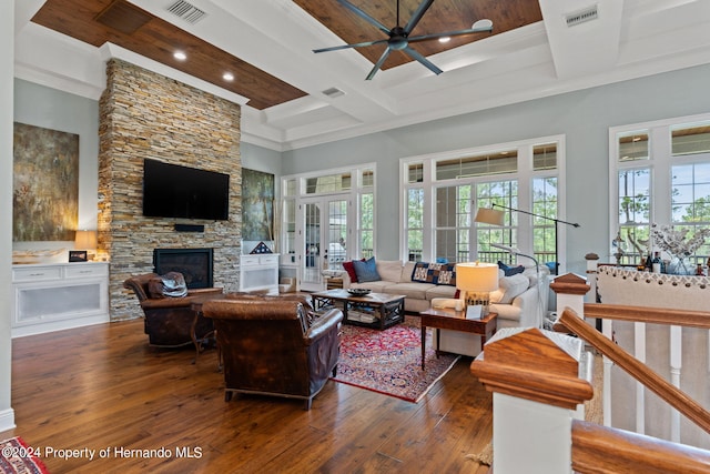 living room featuring a stone fireplace, dark hardwood / wood-style flooring, a towering ceiling, coffered ceiling, and ceiling fan