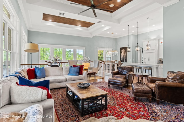 living room with a high ceiling, ceiling fan with notable chandelier, coffered ceiling, and ornamental molding