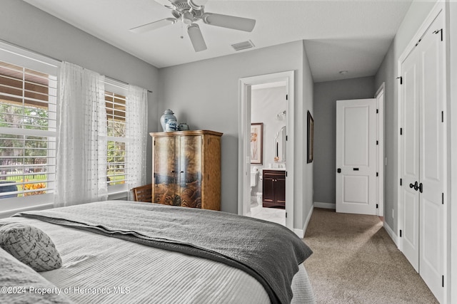 bedroom with light colored carpet, ceiling fan, ensuite bath, and a closet