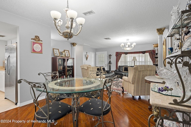 dining area with ornate columns, hardwood / wood-style floors, a notable chandelier, and a textured ceiling