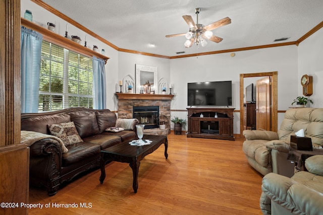 living room featuring a stone fireplace, a textured ceiling, ceiling fan, crown molding, and light wood-type flooring