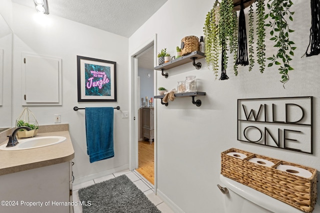 bathroom featuring tile patterned flooring, vanity, a textured ceiling, and toilet