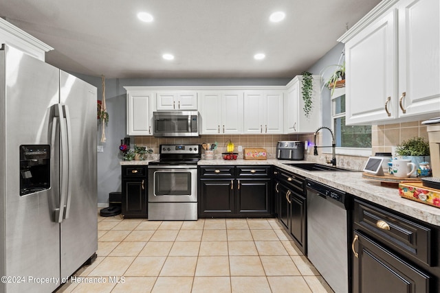 kitchen with stainless steel appliances, sink, light tile patterned flooring, light stone countertops, and white cabinetry