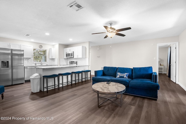 living room with a textured ceiling, dark wood-type flooring, and ceiling fan