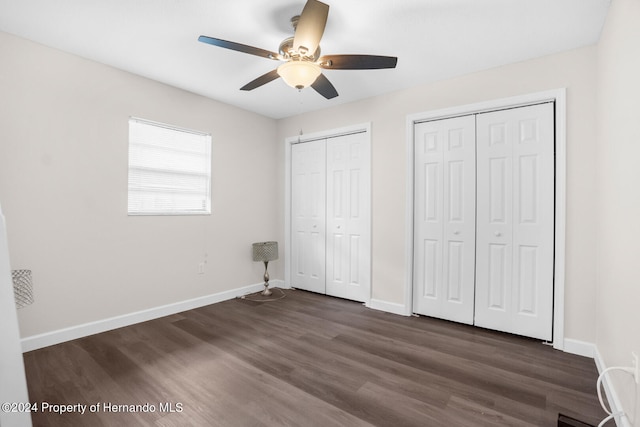 unfurnished bedroom with dark hardwood / wood-style flooring, two closets, and ceiling fan