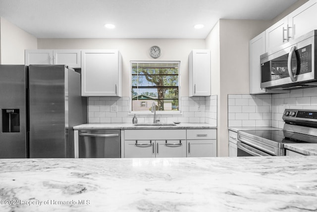 kitchen with white cabinets, appliances with stainless steel finishes, sink, and light stone counters