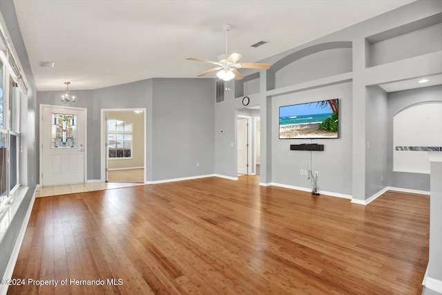 unfurnished living room featuring ceiling fan with notable chandelier, vaulted ceiling, and light hardwood / wood-style flooring