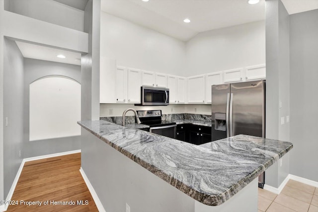 kitchen with kitchen peninsula, appliances with stainless steel finishes, light wood-type flooring, light stone countertops, and white cabinetry