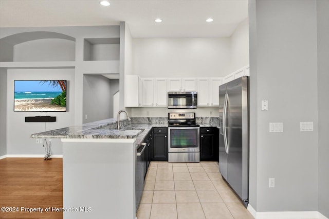 kitchen featuring kitchen peninsula, sink, appliances with stainless steel finishes, light stone counters, and white cabinetry