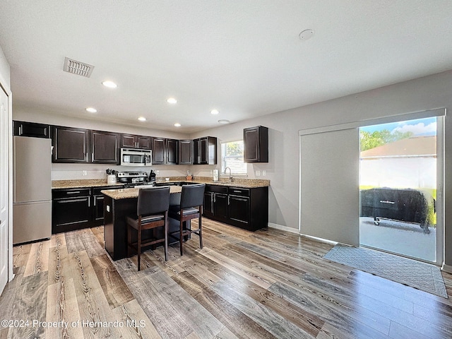 kitchen with appliances with stainless steel finishes, a kitchen bar, light hardwood / wood-style floors, and a center island