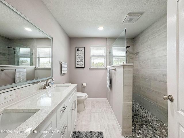 bathroom featuring tiled shower, vanity, a textured ceiling, and toilet