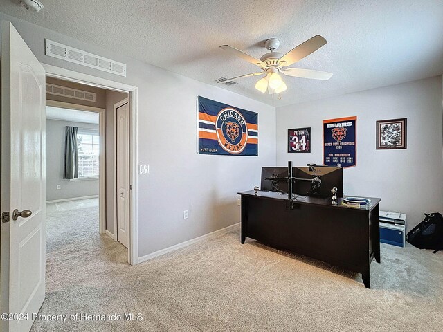 carpeted home office featuring a textured ceiling and ceiling fan