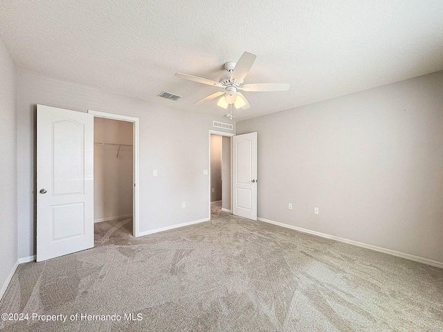 unfurnished bedroom featuring a closet, a spacious closet, carpet floors, a textured ceiling, and ceiling fan