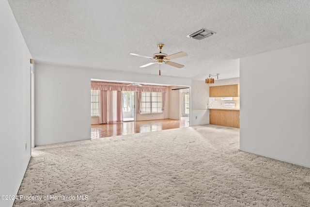 unfurnished living room featuring ceiling fan, a textured ceiling, and light carpet