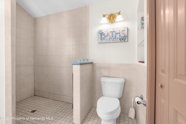 bathroom featuring tile patterned floors, toilet, a tile shower, and tile walls