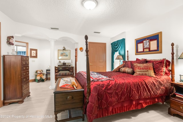 bedroom featuring a textured ceiling, light hardwood / wood-style flooring, and decorative columns