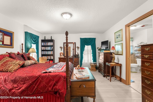 bedroom featuring ensuite bathroom, hardwood / wood-style flooring, and a textured ceiling