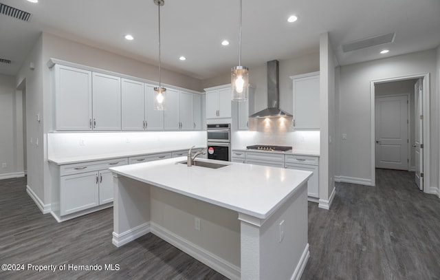 kitchen featuring white cabinets, sink, wall chimney exhaust hood, and hanging light fixtures