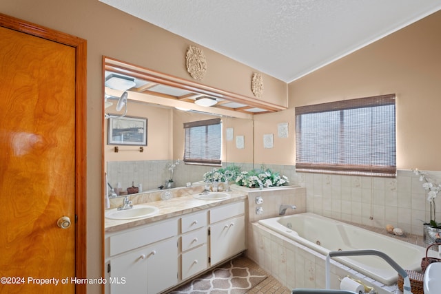 bathroom featuring tiled tub, vanity, a textured ceiling, vaulted ceiling, and tile patterned flooring