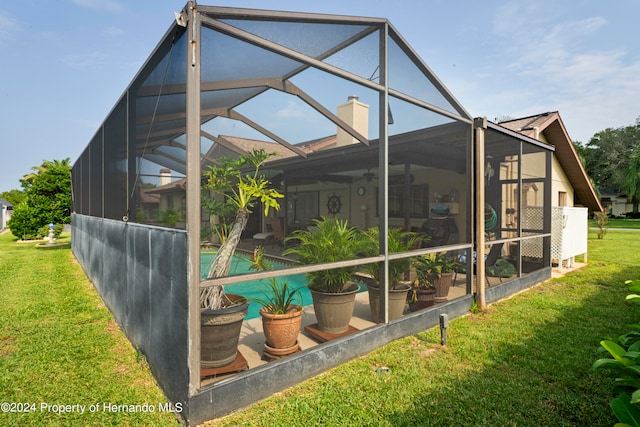 rear view of house with a lanai, a lawn, and a swimming pool