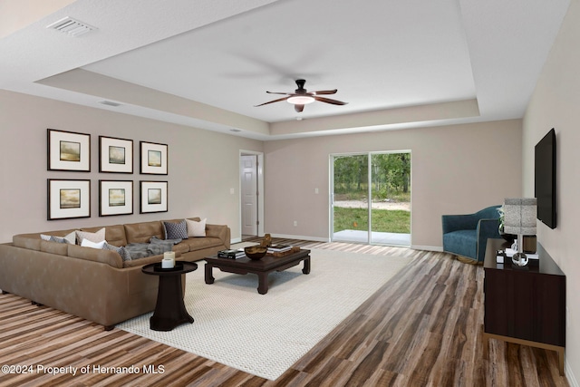 living room with hardwood / wood-style floors, ceiling fan, and a tray ceiling