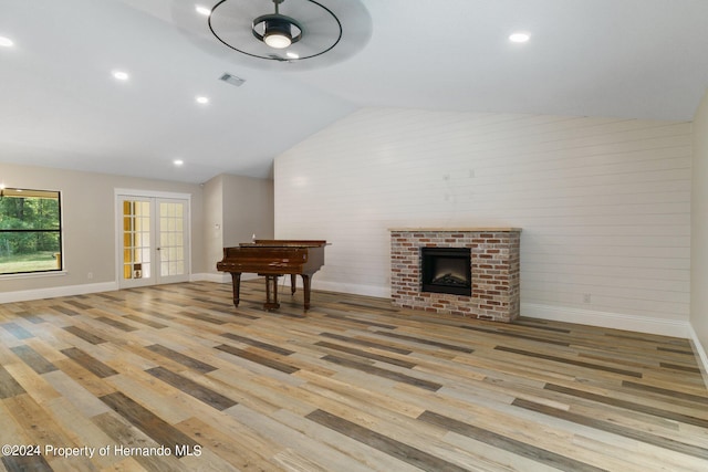 living room with a brick fireplace, light hardwood / wood-style floors, french doors, and lofted ceiling