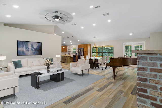 living room with ceiling fan with notable chandelier, light hardwood / wood-style floors, and vaulted ceiling