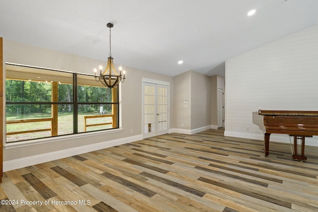 unfurnished dining area with light wood-type flooring, vaulted ceiling, a notable chandelier, and french doors