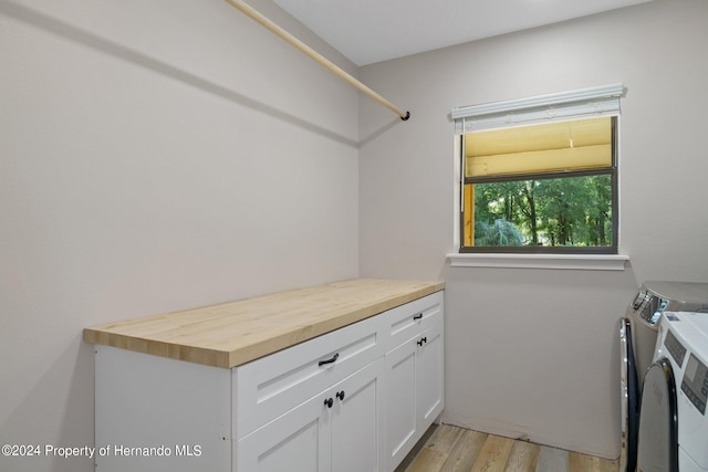 clothes washing area with washing machine and clothes dryer, cabinets, and light hardwood / wood-style flooring