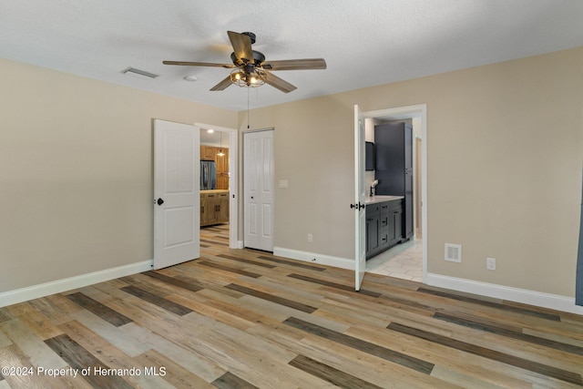 unfurnished bedroom featuring ensuite bathroom, ceiling fan, a textured ceiling, light hardwood / wood-style flooring, and a closet