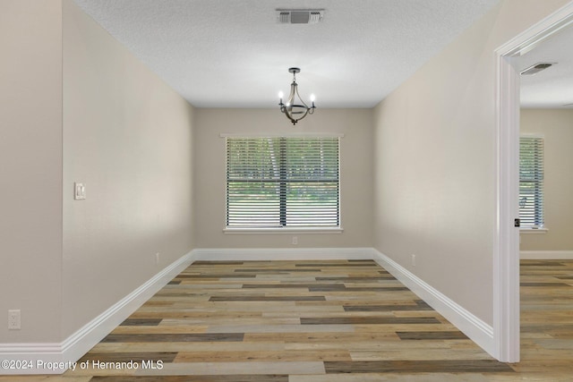 unfurnished dining area featuring hardwood / wood-style floors, a notable chandelier, and a textured ceiling