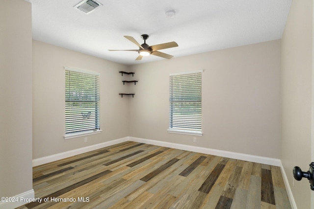 empty room featuring a wealth of natural light, wood-type flooring, and ceiling fan